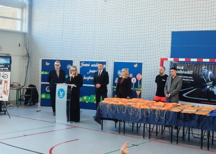 Zdjęcie 4. Na zdjęciu od lewej: Pan Artur Rola – Dyrektor Delegatury Urzędu Marszałkowskiego Województwa Mazowieckiego w Wołominie, (z mikrofonem) przemawiająca do uczestników spotkania Pani Katarzyna Szymańska – przedstawicielka Urzędu Marszałkowskiego Województwa Mazowieckiego w Warszawie, Pan Sylwester Winek – Wójt Gminy Kołbiel, Pani Małgorzata Szerszeń – Dyrektor Szkoły SP w Kołbieli, Pan Piotr Żak - ratownik medyczny z SPZOZ MEDITRANS w Warszawie, Pan Kacper Wojdalski – przedstawiciel Urzędu Marszałkowskiego Województwa Mazowieckiego w Warszawie oraz sierżant Piotr Świątek – Policjant z Komendy Powiatowej Policji w Otwocku. (zdjęcie źródło: WORD w Warszawie).