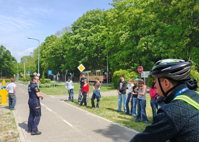 Zdjęcie 3. Uuczniowie I Liceum Ogólnokształcącego im. Maharadży Digvijay Sinhji w Warszawie - uczestnicy „szkolenia praktycznego” na Kartę rowerową oraz Pan Sławomir Bakalarski (w szelkach odblaskowych)  – Egzaminator z WSiBRD prowadzący zajecia na terenie Miasteczka Ruchu Drogowego przy ul. Sołtyka 8 w Warszawie. (Zdjęcie źródło: WORD w Warszawie).